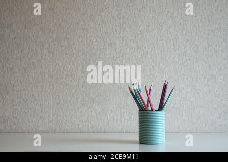 Nahaufnahme von Pastellstiften im blauen Glas Der Schreibtisch im grauen Wandhintergrund Stockfoto