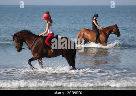 Zwei Reiter kühlen ihre Pferde im Meer bei East Wittering in West Sussex ab. Stockfoto