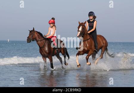 Zwei Reiter kühlen ihre Pferde im Meer bei East Wittering in West Sussex ab. Stockfoto