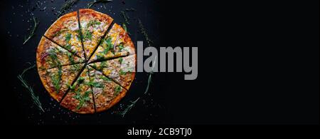 Leckere frisch gebackene Pizza mit Tomaten und Basilikum auf schwarzem Hintergrund. Blick von oben auf heiße leckere Pizza. Mit Kopierplatz für Text. Flach liegend. Banner Stockfoto