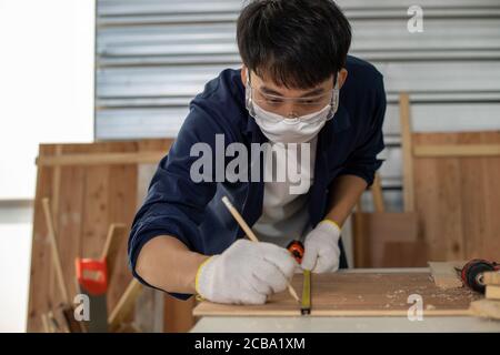 Asian man Carpenter arbeitet mit technischem Zeichnen oder Baupapier, das auf einer Werkstatt mit Zimmermannswerkzeugen und Holz zu Hause liegt Stockfoto