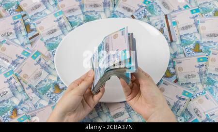 Zählen Sie Geld in Tenge. Viele kasachische Tenge auf einem weißen Teller. Die nationale Währung von Kasachstan. Gehalt in Tenge. Um das Budget zu kürzen. Stockfoto