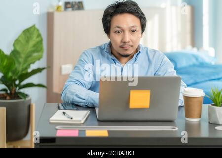 Asiatischer Geschäftsmann mit Technologie Laptop und Arbeit von zu Hause aus Mit Überraschungsaktion im Schlafzimmer des Hauses durch Videokonferenz Anruf, Start-ups und Busine Stockfoto