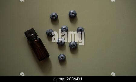 Eine Flasche ätherisches Heidelbeeröl und frische Heidelbeeren Auf dunkelgrünem Hintergrund Stockfoto