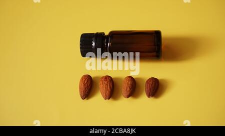Flasche Mandelöl und Mandeln auf gelbem Hintergrund - Flasche und Reihe von Nüssen Stockfoto