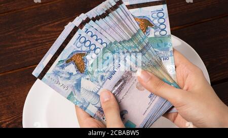 Zählen Sie Geld in Tenge. Viele kasachische Tenge auf einem weißen Teller. Die nationale Währung von Kasachstan. Gehalt in Tenge. Um das Budget zu kürzen. Stockfoto