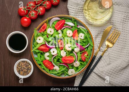 Mediterranes Diät-Menü Konzept gesunder Salat aus frischem Gemüse - Tomaten, Rucola, lila Zwiebeln in Teller, Sesam, Sojasauce, Messer, Gabel Stockfoto