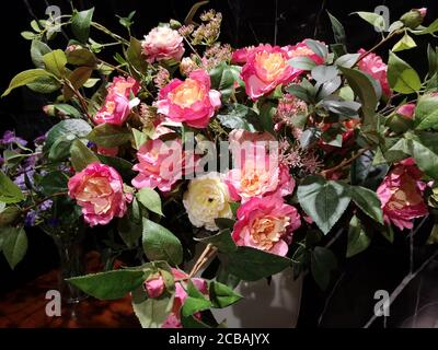 Schönes Bouquet von rosa und gelben Rosen in einer weißen Vase auf Holztisch schwarzem Marmor Hintergrund, künstliche Blumen Stockfoto