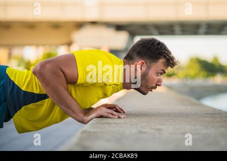 Der junge Mann trainiert draußen. Er macht Liegestütze. Stockfoto