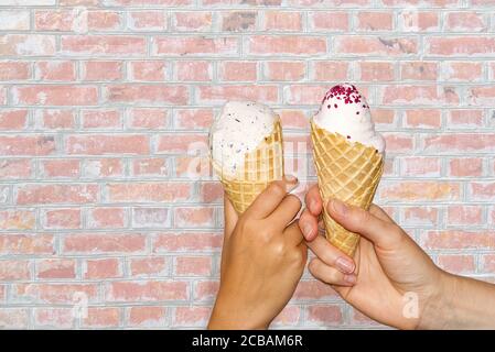 Mutter und Tochter Hände hält Eis Mais mit Milch Eis Begasung alten roten Ziegelwand. Zwei Hände hält Eis. Stockfoto