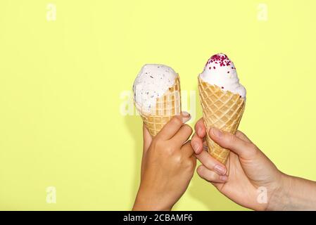 Mutter und Tochter Hände hält Eis Mais mit Milch Eis. Isoliert auf einem gelben Hintergrund. Zwei Hände hält Eis. Stockfoto