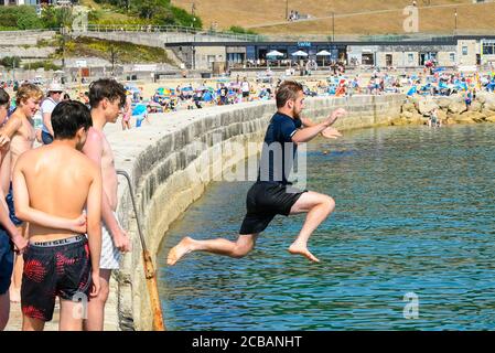 Lyme Regis, Dorset, Großbritannien. August 2020. Wetter in Großbritannien. Schwimmer tauchen in das Meer von der Cobb Harbour Wand im Badeort Lyme Regis in Dorset an einem weiteren heißen sonnigen Tag, wie die Hitzewelle weiter. Bild: Graham Hunt/Alamy Live News Stockfoto