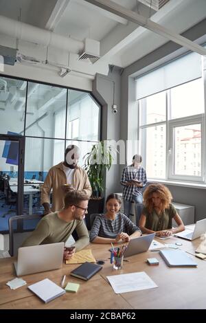Erfolgreiches Team im Coworking Space. Vertikale Aufnahme von multirassischen Kollegen kommunizieren, teilen frische Ideen während der Zusammenarbeit in der modernen Stockfoto