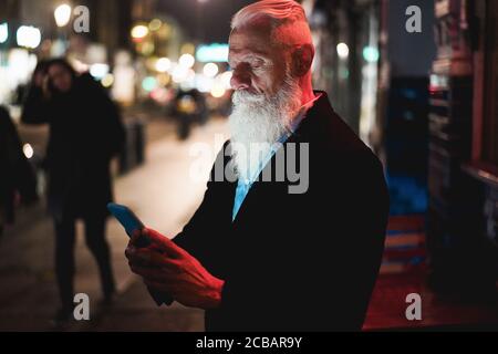 Stilvoller Senior mit Smartphone in der Stadt Straße mit stehen Bokeh Lichter im Hintergrund - Hipster Influencer Spaß mit Technologietrends – T Stockfoto