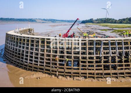 Arbeiter des Canal and River Trust, die bei Ebbe abseilen, um Reparaturen am hölzernen Pier am Eingang zum Sharpness New Dock am Fluss Severn in Gloucestershire durchzuführen. Wasserstraßen wohltätige Canal und River Trust verwenden einen Spinnenkran, um in greenheart Eichendielen, die an Ort und Stelle von einem Team gesenkt werden auf Seilen über dem schlammigen Flussbett bei Ebbe aufgehängt gebracht bringen. Stockfoto