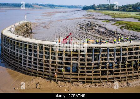 Arbeiter des Canal and River Trust, die bei Ebbe abseilen, um Reparaturen am hölzernen Pier am Eingang zum Sharpness New Dock am Fluss Severn in Gloucestershire durchzuführen. Wasserstraßen wohltätige Canal und River Trust verwenden einen Spinnenkran, um in greenheart Eichendielen, die an Ort und Stelle von einem Team gesenkt werden auf Seilen über dem schlammigen Flussbett bei Ebbe aufgehängt gebracht bringen. Stockfoto