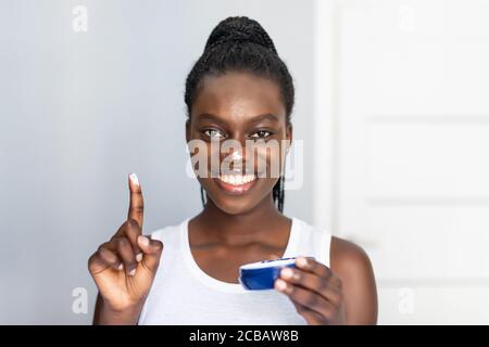 Schwarzes Mädchen kümmern sich um ihre schöne Haut. Junge afrikanische Frau Anwendung Feuchtigkeitscreme auf ihr Gesicht. Stockfoto