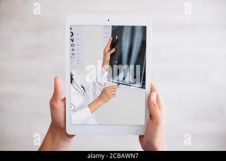 Person, die eine Tablette hält und einen Arzt zeigt, der die eines Patienten untersucht Röntgenstrahlen in einem Krankenhaus Stockfoto