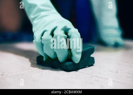 Person, die Gummihandschuhe trägt und die Handschuhe mit einem Schwamm reinigt Stockfoto