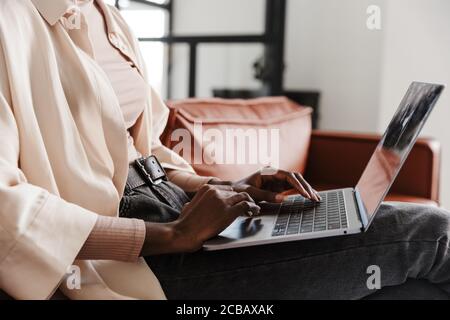 Zugeschnittenes Bild einer jungen Frau, die drinnen auf dem Sofa sitzt Zu Hause, während Sie mit einem Laptop arbeiten Stockfoto