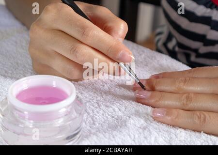 Frau Anwendung rosa Gel Nägel polieren auf einem Finger auf einem weißen Handtuch zu Hause. Beauty und Maniküre Konzept Stockfoto