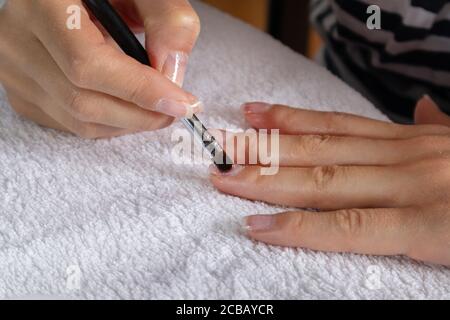 Frau Anwendung Schutzgel Nägel polieren auf einem Finger auf einem weißen Handtuch zu Hause. Beauty und Maniküre Konzept Stockfoto