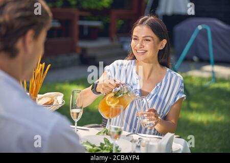 Glücklich lächelnd Frau trägt Bluse Gießen orange Limonade im Glas Stockfoto