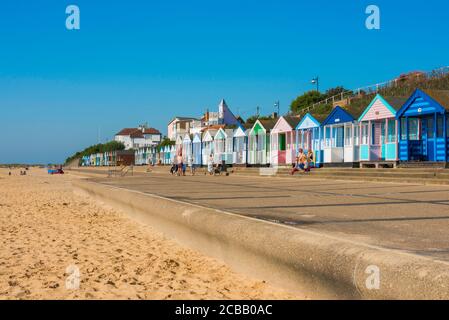 Suffolk Coast UK, Blick im Sommer auf die Menschen sitzen vor bunten Strandhütten entlang der Küste in Southwold an der Suffolk Küste, England, Großbritannien Stockfoto