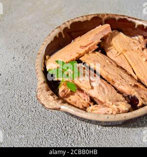 Nahaufnahme von einigen Stücken spanischer Bonito en aceit, einem Makrelenartigen Fisch in Öl, in einem Steingutteller, auf einer strukturierten grauen Oberfläche Stockfoto