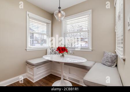 Ein kleines Frühstücksbuch in einem Wohnhaus. Der Bereich verfügt über Sitzbänke, Kissen und Kissen mit einem kleinen weißen ovalen Tisch mit Blumen darauf. Stockfoto