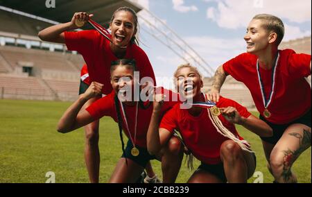 Fußballspielerinnen jubeln nach der Spielliga zusammen. Fußballmannschaft mit Medaillen, die zusammen schreien, nachdem sie den Wettbewerb gewonnen haben. Stockfoto