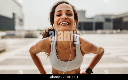 Fitness-Frau, die Ohrhörer trägt, in die Kamera schaut und lächelt. Fröhliche Läuferin in Sportbekleidung. Stockfoto