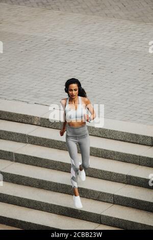 Hochwinkelansicht einer sportlichen Frau, die draußen die Stufen hinunterläuft. Hündin in Sportswear Laufen am Morgen. Stockfoto