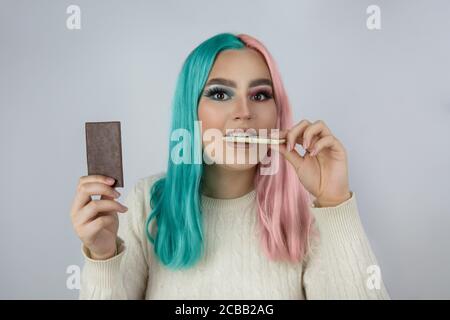 Junge Frauen in gefärbten Haaren rosa und blau Farben und Halten auf einer Hand Milchschokolade und eine andere Hand weiß Schokolade Stockfoto
