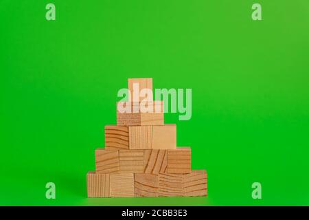 Pyremid Konstruktion aus Holzwürfeln auf grünem Hintergrund mit Kopierraum. Mockup Komposition für Design. Stockfoto