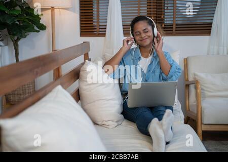 Lächelnde Frau mit Kopfhörer und Laptop zu Hause sitzen. Stockfoto