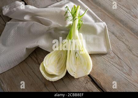 Frische rohe Fenchelknolle halbiert, gesundes Gemüse zum Kochen eines mediterranen Sommergerichtes auf Serviette und rustikalen Holzplanken, Kopierraum, ausgewählter Fokus, Stockfoto