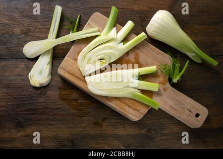 Geschnittener roher Fenchel auf einem Schneidebrett und einem dunklen rustikalen Holztisch, gesundes Gemüse, Kopierraum, flaches Lay, Hochwinkelansicht von oben Stockfoto