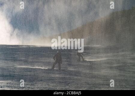 Skifahrer und Snowboarder, die auf der Bellow Working Snow Gun reiten. Schwere verschneite Wolke schwimmt auf der Piste in Italien Skigebiet. Stockfoto