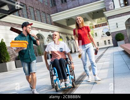 Eine Gruppe von Freunden, die am Sommertag auf der Straße der Stadt spazieren gehen. Behinderter, behinderter Mann mit seinen Freunden, die Spaß haben. Inklusion und Diversity-Konzept, normale Lebensweise von besonderen Gruppen der Gesellschaft. Stockfoto