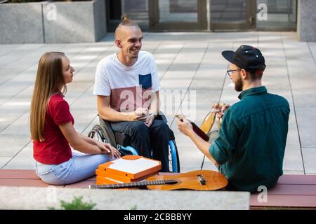 Eine Gruppe von Freunden, die am Sommertag auf der Straße der Stadt spazieren gehen. Behinderter, behinderter Mann mit seinen Freunden, die Spaß haben. Inklusion und Diversity-Konzept, normale Lebensweise von besonderen Gruppen der Gesellschaft. Stockfoto