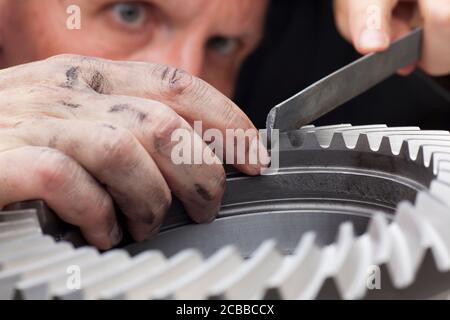 Nahaufnahme der Hände eines Mechanikers, der ein Zahnrad repariert Mit einer Raspel - im Hintergrund das Gesicht von Die Werkstatt Stockfoto