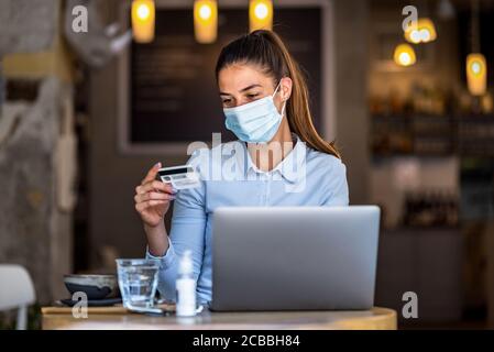 Porträt der jungen Geschäftsfrau trägt Maske beim Online-Shopping und Zahlung mit Kreditkarten. Neuer normaler Lebensstil während der covid-19 Pandemie. Stockfoto