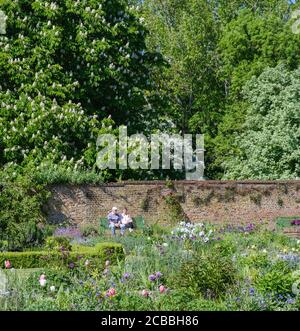 Ein älteres Paar sitzt auf einer Bank im Eastcote House Walled Garden, zwischen Bäumen und Blumen. Hillingdon, London Stockfoto