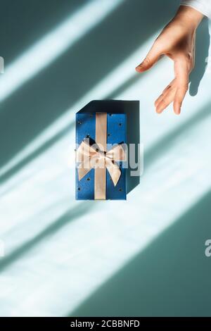 Ein Geschenk in der Mitte des Tisches und die Hand einer Frau, die nach ihm greift. Flachbild. Stockfoto