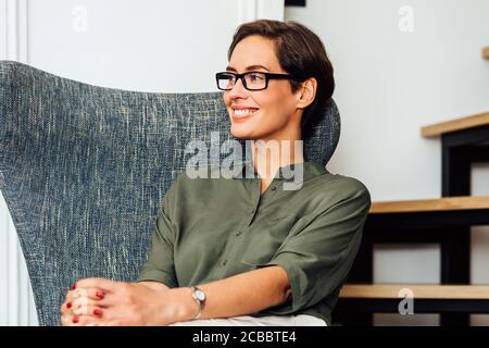 Selbstbewusste Geschäftsfrau sitzt auf einem Sessel in ihrer Wohnung und sucht Weg Stockfoto