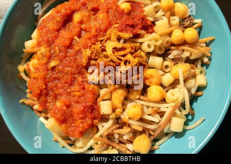 Berühmte traditionelle arabische, ägyptische Gericht - Koshari. National Kushari in einem türkisfarbenen Teller, Nahaufnahme . Draufsicht. Koshari Hintergrund Stockfoto