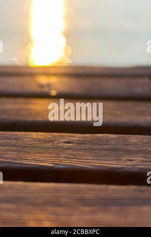 Holzdeck einer Anlegestelle am Gardasee. Die Sonne spiegelt sich im Wasser. Das Holz ist warm, braun gefärbt. Stockfoto