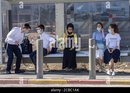 Jerusalem, Israel - 6. August 2020: Junge jüdische orthodoxe Menschen in COVID-Masken in einer Bushaltestelle in Jerusalem. Stockfoto