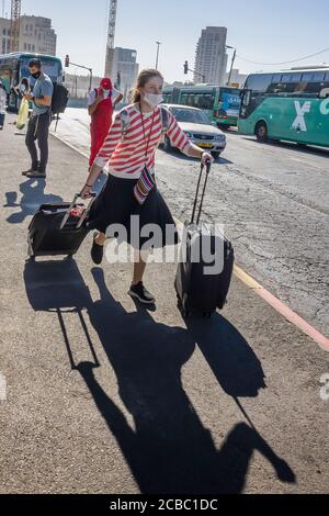 Jerusalem, Israel - 6. August 2020: Ein jüdisch-orthodoxes Mädchen, das eine COVID Maske trägt, läuft, um ihren Bus auf einer Jerusalemer Straße zu fangen. Stockfoto